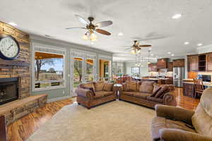 Living area with wood finished floors, ornamental molding, a stone fireplace, ceiling fan, and recessed lighting