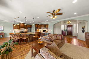 Living area with ornamental molding, arched walkways, light wood finished floors, a chandelier, and recessed lighting