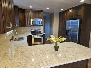 Kitchen featuring dark brown cabinetry, stainless steel appliances, light stone countertops, recessed lighting, and a peninsula