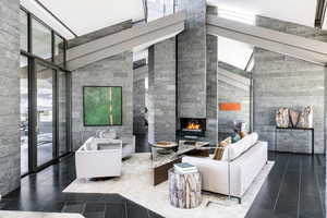 Living area with high vaulted ceiling, a lit fireplace, and a wall of windows