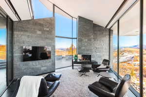 Living area featuring an outdoor stone fireplace, a wall of windows, a mountain view, and vaulted ceiling