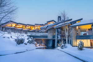 View of snowy exterior with a balcony, a chimney, and stone siding