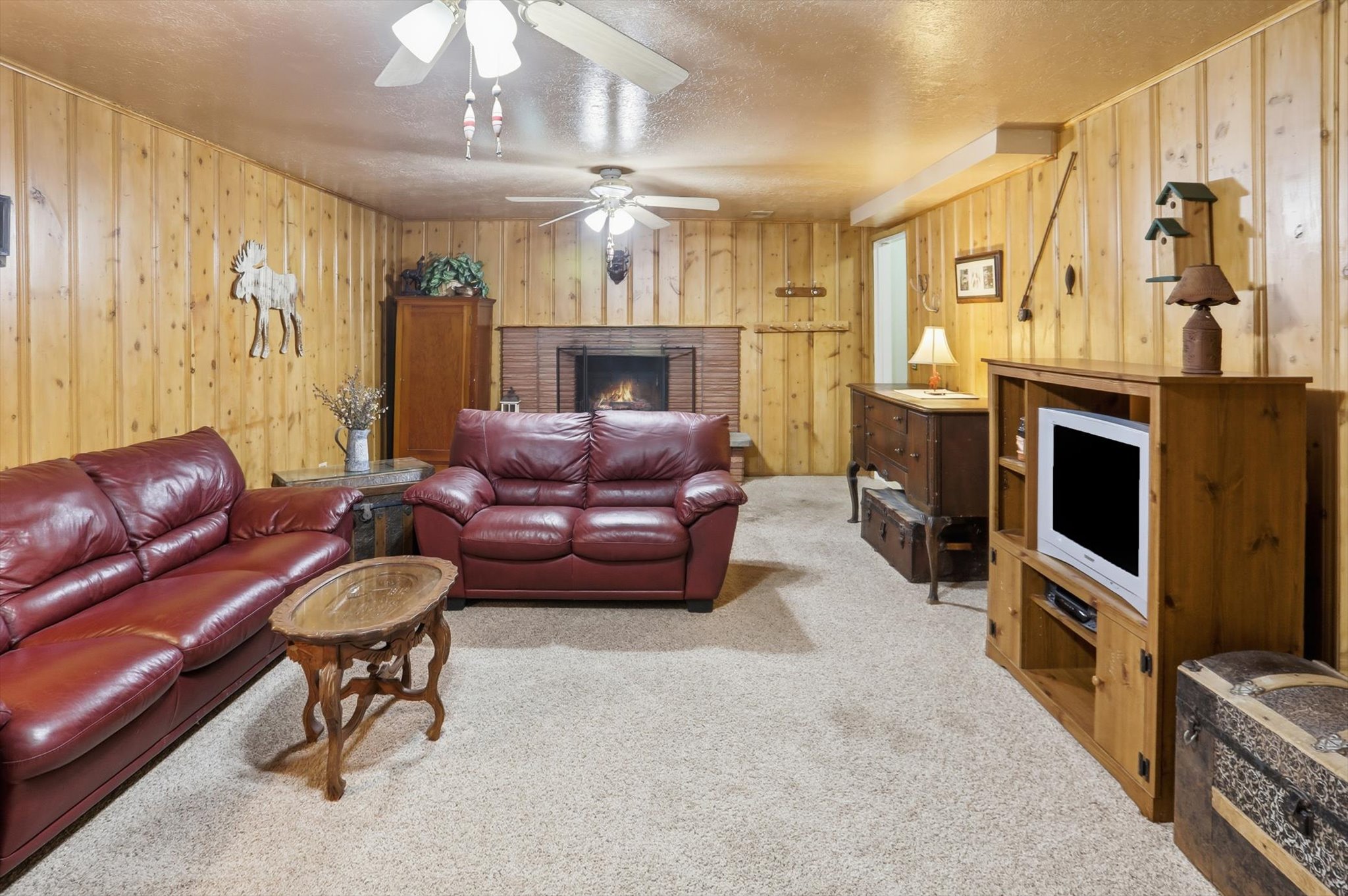 Living area featuring a brick fireplace, light colored carpet, a textured ceiling, and wooden walls