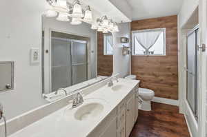 Full bath with wooden walls, a stall shower, double vanity, dark wood-style flooring, and a chandelier