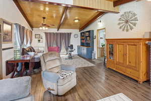 Living room with ceiling fan, brick wall, dark wood finished floors, and wooden ceiling