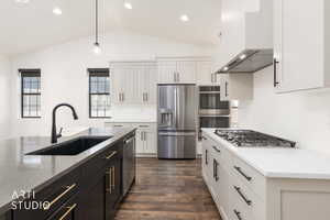 Kitchen featuring appliances with stainless steel finishes, dark stone countertops, custom range hood, hanging light fixtures, and lofted ceiling