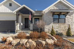 View of front facade with stone siding, covered porch, board and batten siding, driveway, and an attached garage