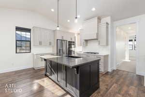 Kitchen with white cabinetry, an island with sink, decorative light fixtures, dark wood-style floors, and lofted ceiling