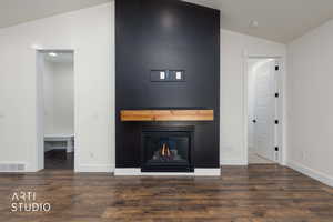 Unfurnished living room with lofted ceiling, dark wood finished floors, and a warm lit fireplace