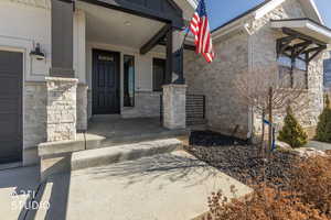 Doorway to property with stone siding, a porch, and a garage
