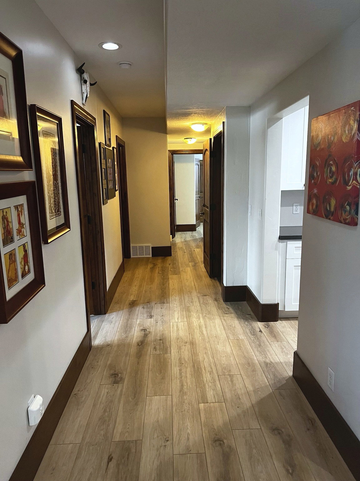 Long hallway featuring wood-finish plank flooring, dark wood trim, recessed lighting, and white walls
