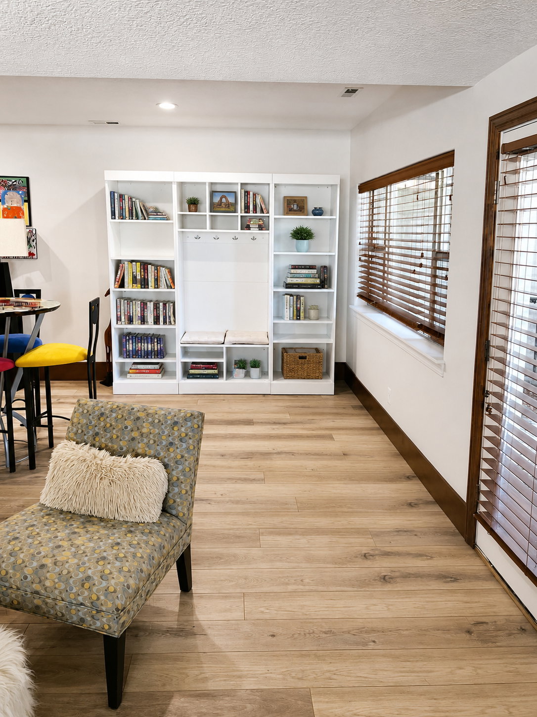 Expansive wood-finish flooring throughout the room, featuring a built-in white shelving unit with integrated coat hooks and bench seating