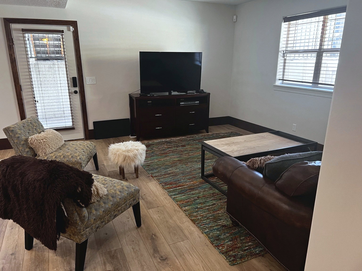 Living area featuring wood-finish flooring, a white-framed window with blinds, and a white paneled door with glass inserts and blinds