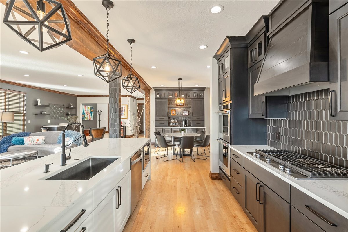 Kitchen showcasing functional excellence and custom design, featuring elegant pendant lighting, light wood-style flooring, an open-concept layout, a bespoke range hood, and luminous light-stone countertops.