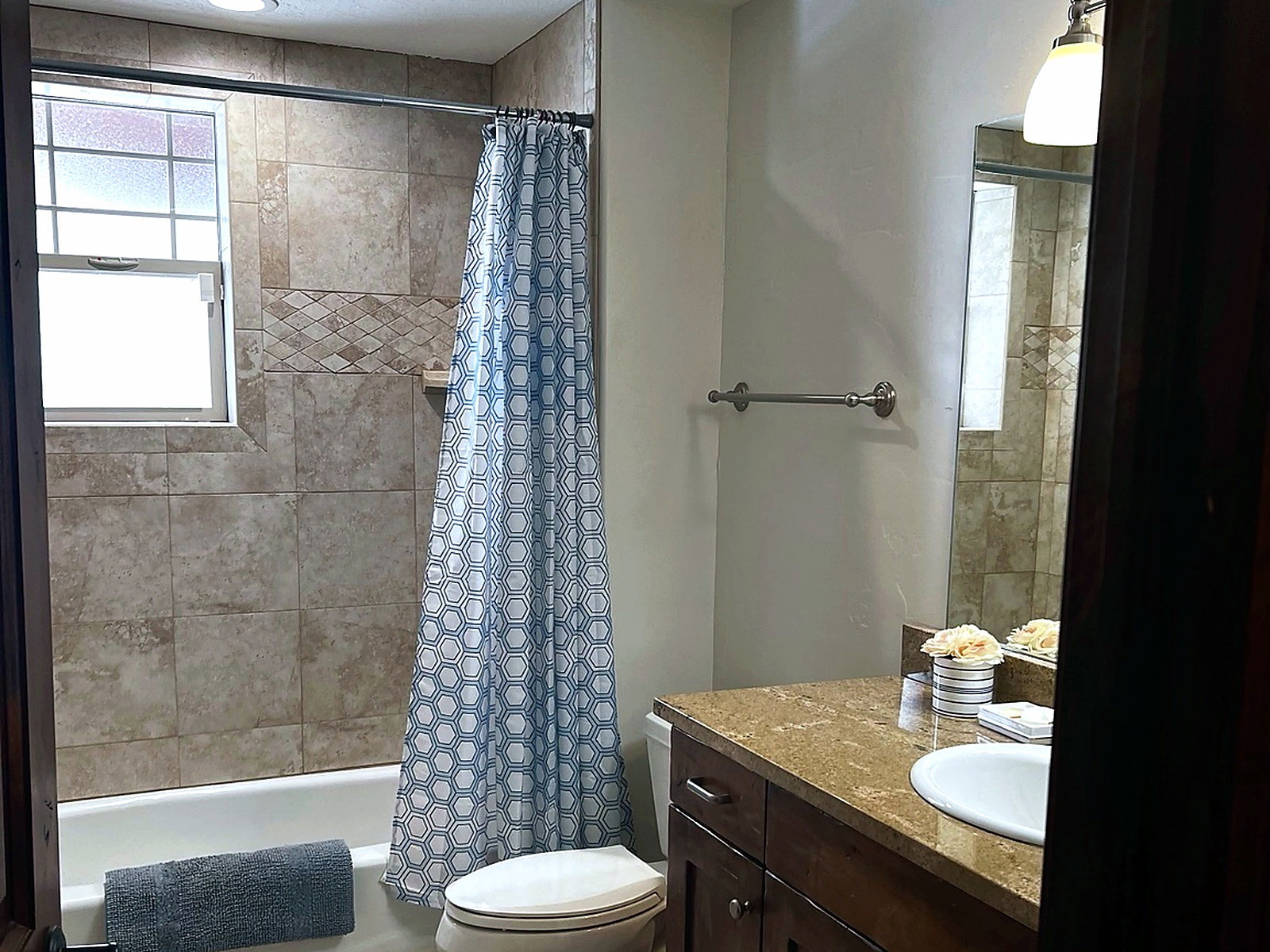 Bathroom featuring a shower-over-tub combination with tile surround, a built-in window, and a single vanity with a granite countertop