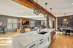 Expansive view of the kitchen showcasing light wood-style flooring, elegant pendant fixtures, luminous light-stone countertops, and a generous sink-centered island within an open-concept layout.