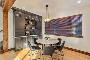 Dining area featuring light wood-style flooring, softly integrated recessed lighting, and a custom built-in cabinet offering exceptional storage and display space.