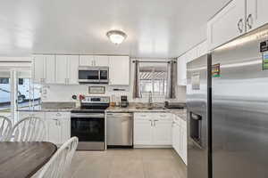 Kitchen featuring appliances with stainless steel finishes, white cabinets, light stone counters, and light tile patterned flooring