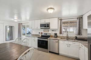 Kitchen with appliances with stainless steel finishes, white cabinets, light stone counters, light tile patterned flooring, and healthy amount of natural light