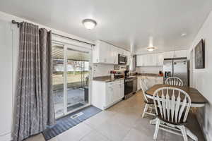 Kitchen with appliances with stainless steel finishes, white cabinetry, light tile patterned flooring, and dark stone countertops
