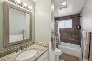 Full bathroom with vanity, shower / bathtub combination with curtain, and a textured ceiling