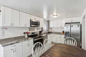 Kitchen featuring appliances with stainless steel finishes, white cabinetry, and dark stone counters