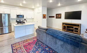 Kitchen featuring stainless steel appliances, open floor plan, an island with sink, a textured ceiling, and white cabinetry