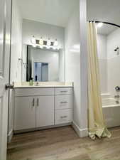 Bathroom with shower / bath combination with curtain, light wood-style flooring, and vanity