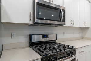 Kitchen with appliances with stainless steel finishes, white cabinets, and light stone counters