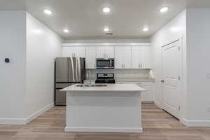 Kitchen featuring stainless steel appliances, light wood-type flooring, white cabinetry, a kitchen island with sink, and recessed lighting