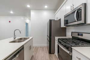 Kitchen featuring stainless steel appliances, white cabinets, light wood-style flooring, light stone countertops, and recessed lighting