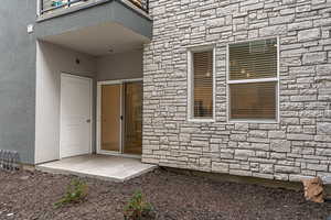 View of exterior entry with stone siding, a patio area, and stucco siding