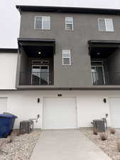 Rear view of house with a balcony, stucco siding, a garage, and driveway