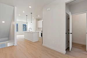 Kitchen featuring white cabinets, an island with sink, pendant lighting, light wood finished floors, and recessed lighting