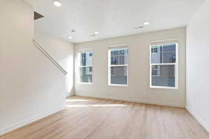 Spare room featuring light wood-style flooring, a textured ceiling, healthy amount of natural light, and recessed lighting