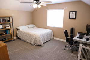 Carpeted bedroom with vaulted ceiling, an office area, ceiling fan, and radiator