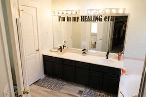 Full bathroom with double vanity, a walk in closet, a tub to relax in, and light wood-style floors