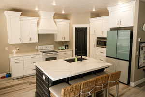 Kitchen with white appliances, a center island with sink, light stone counters, a breakfast bar, and custom exhaust hood