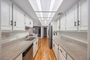 Kitchen with light stone counters, white cabinetry, appliances with stainless steel finishes, and light wood-type flooring