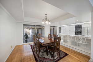 Dining room with light wood-style flooring, a chandelier, a raised ceiling, and recessed lighting