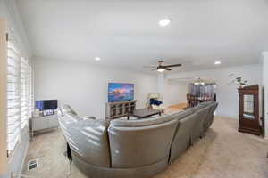 Living room featuring light carpet, ornamental molding, a ceiling fan, recessed lighting, and a chandelier
