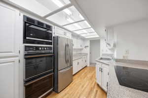 Kitchen featuring white cabinetry, black appliances, light wood-style flooring, and light stone countertops