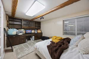 Bedroom featuring beam ceiling, light colored carpet, and built in study area