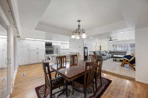 Dining room with a chandelier, light wood-type flooring, recessed lighting, ceiling fan, and a tray ceiling