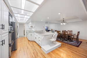 Kitchen featuring a peninsula, decorative light fixtures, white cabinets, light wood-type flooring, and recessed lighting