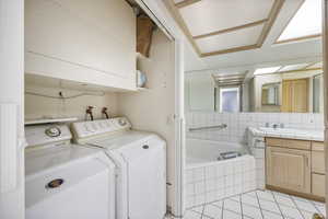 Bathroom featuring vanity, tiled bath, separate washer and dryer, and light tile patterned floors