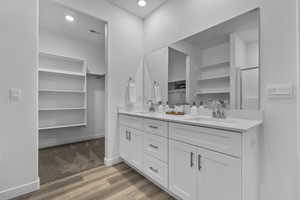 Bathroom featuring a spacious closet, double vanity, light wood-type flooring, and recessed lighting