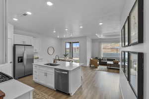 Kitchen with stainless steel appliances, a kitchen island with sink, white cabinets, open floor plan, and light wood-style floors