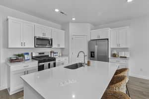 Kitchen with dark wood-style flooring, appliances with stainless steel finishes, white cabinetry, a kitchen breakfast bar, and recessed lighting