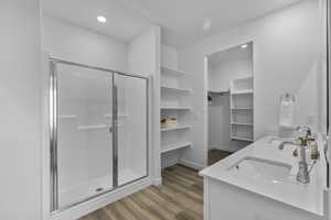 Full bathroom featuring a shower stall, double vanity, dark wood finished floors, a walk in closet, and recessed lighting